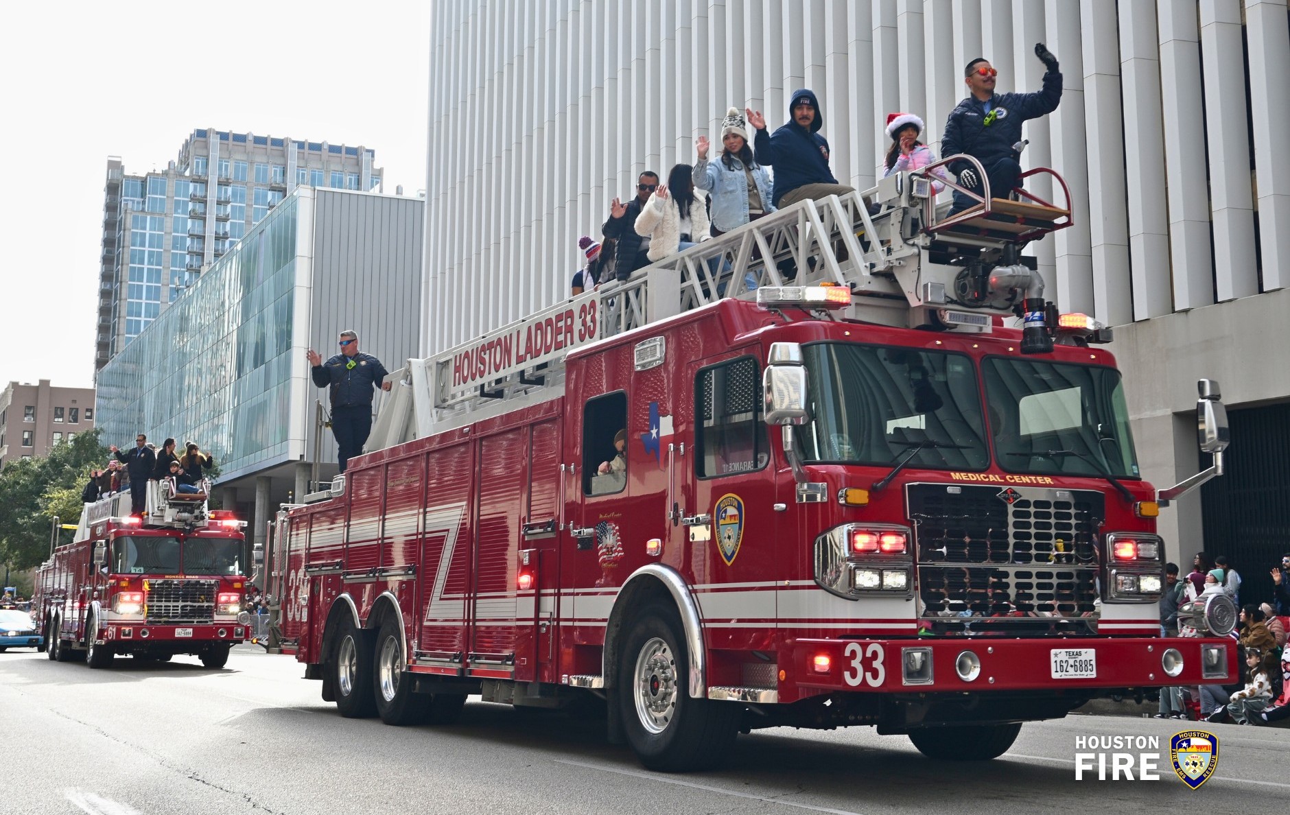 Photo of two HFD ladder trucks with people on top in downtown houston parade